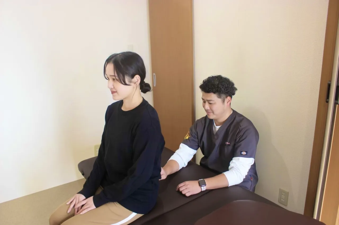 座った姿勢で背骨のカーブを確認するスタッフ